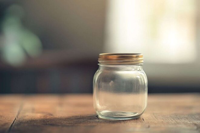 Gros plan d'un bocal en verre vide posé sur une table en bois, avec une lumière naturelle douce qui l'éclaire.